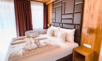 A modern bedroom with a wooden ceiling and stylish bed. The large windows provide plenty of daylight.