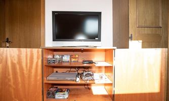 A television is on a wooden cabinet with open doors. Below are game consoles and DVDs.