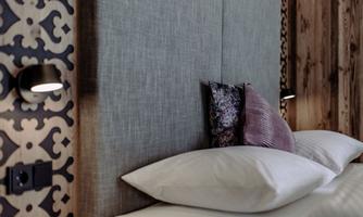 A modern bedroom with a upholstered headboard and two pillows. The wall is artistically decorated with a geometric pattern.