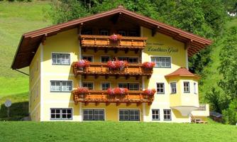 A charming yellow house with wooden decorations and balconies full of flowers. Surrounded by green meadows and mountains.