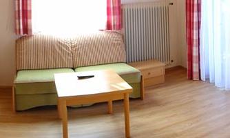 A cozy room with a small kitchen and a living area. There is a window with curtains and a table in the center.