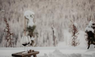 A cozy outdoor area with a hot tub in the snow. On a small table, there are two wine glasses and a snack.