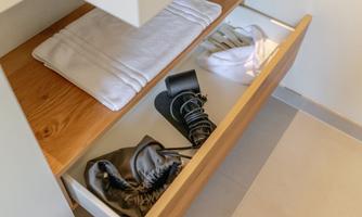 An open drawer with various items. Among them are towels and several types of shoes.
