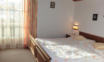 A cozy bedroom with a large bed and soft colors. Warm light streams into the room through the windows.