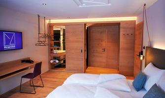 A modern hotel room with a double bed and wood decorations. The room features a TV, a chair, and an inviting atmosphere.