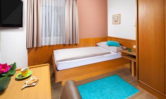 A cozy bedroom with a single bed, a desk, and a television. The room has light walls and a friendly atmosphere.