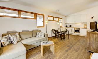 A modern living room with a comfortable couch and a dining table. The open kitchen is bright and inviting, with large windows for plenty of daylight.