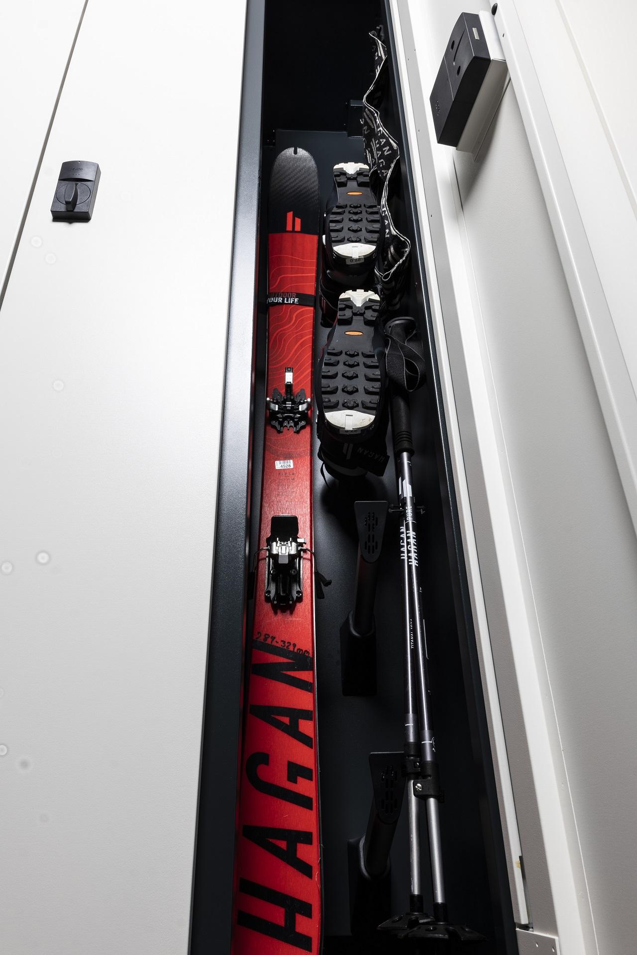 A ski cabinet with red skis, ski boots, and a ski pole. Everything is neatly stored.