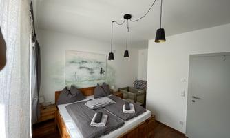 A modern bedroom with a large bed and cozy pillows. Bright walls and a relaxing atmosphere through the windows and the furnishings.