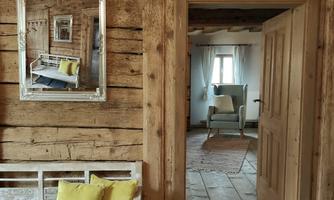 A cozy entrance area with a wooden bench and yellow cushions. Through the open door, you can see a bright room with simple furnishings.