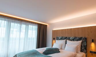 A modern bedroom with a large double bed and elegant furnishings. Plenty of daylight streams through the windows, creating an inviting atmosphere.