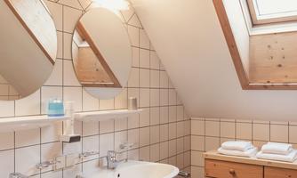 A modern bathroom with two sinks and large mirrors. The room has a bright, friendly atmosphere with wood and tile elements.