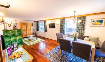 A cozy living space with a dining table and comfortable chairs. Large windows provide plenty of daylight and an inviting atmosphere.