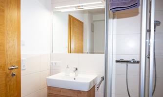 A modern bathroom with a sink, a mirror, and a shower. The walls are brightly tiled and the doors are made of wood.