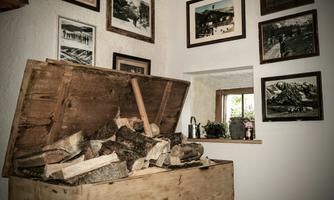 A rustic wooden cupboard with stacked wood stands in a room. Several pictures hanging on the walls depict the surroundings.