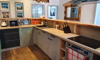 A modern kitchen with wooden shelves and stainless steel appliances. In the background, there are pictures and a large mirror surface.