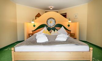 A cozy bedroom with a large bed and an eye-catching headboard design. The walls are painted in light colors, and the carpet is green.