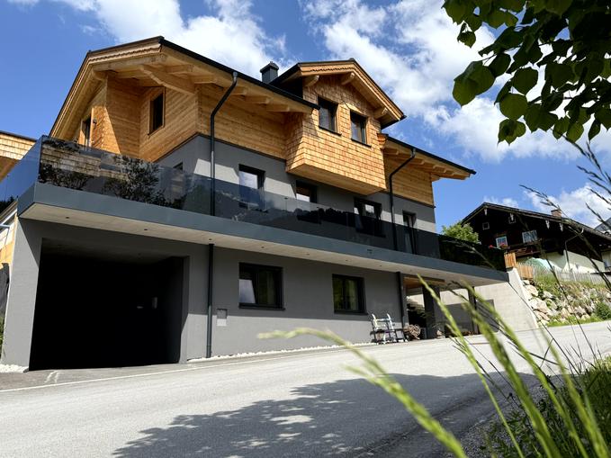 A modern house with wooden cladding and large windows. The sky is blue and there is a tranquil environment.