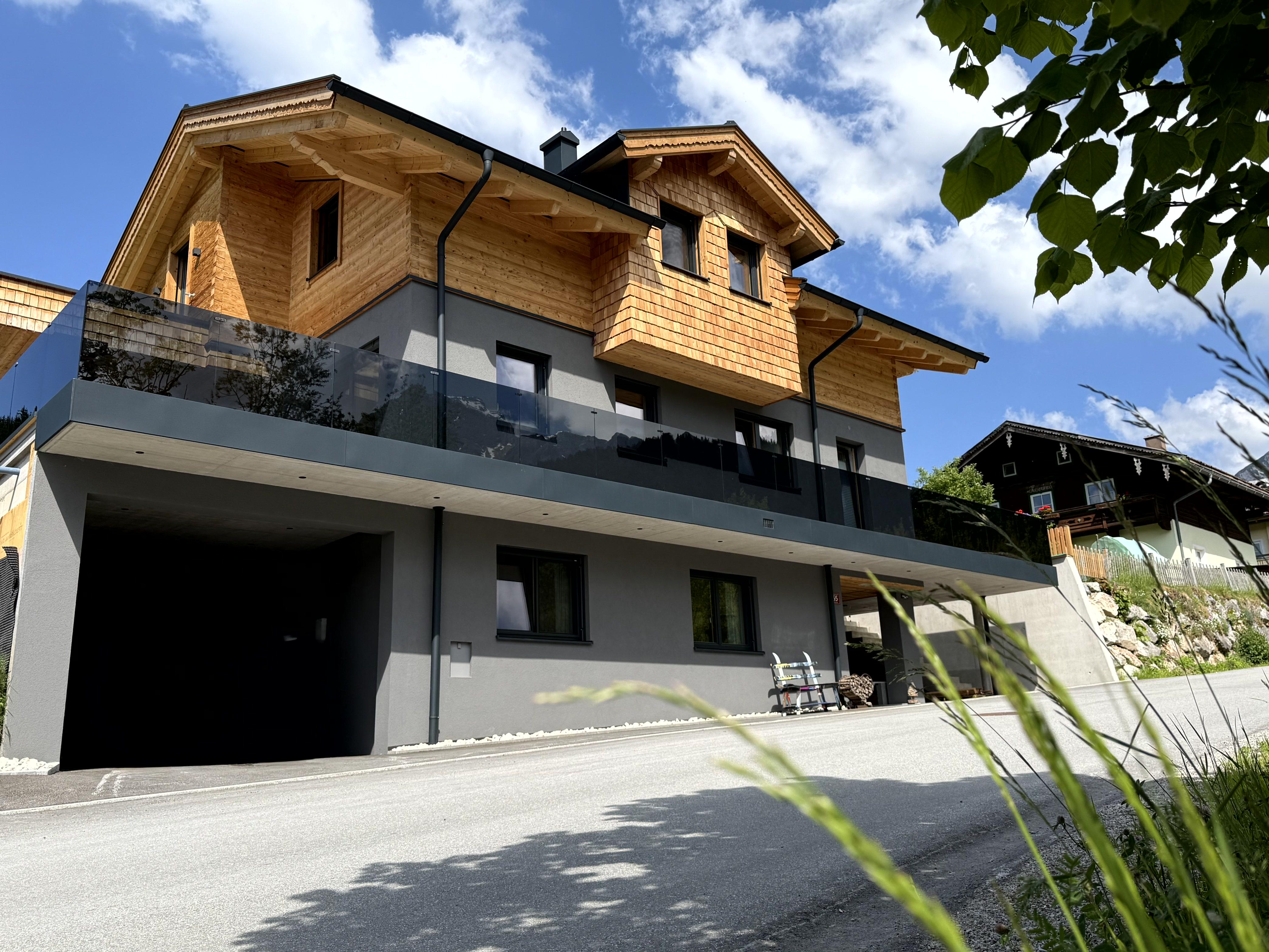 A modern house with wooden cladding and large windows. The sky is blue and there is a tranquil environment.