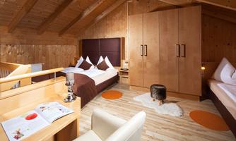 A cozy room with wooden panels and a high ceiling. There are two beds, a small table, and a wardrobe.