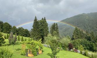 A beautiful garden with green grass and trees. In the background, a rainbow is visible above the mountains.