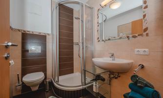 A modern bathroom with a glass shower and a sink. The walls are light tiled and there are fresh towels in blue.