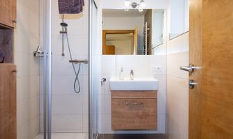 A modern bathroom with a shower and a wooden sink. Bright tiles and ample light create an inviting atmosphere.