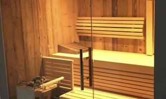 A modern sauna room with wooden paneling and a glass door. Inside, there are wooden benches and sauna accessories.