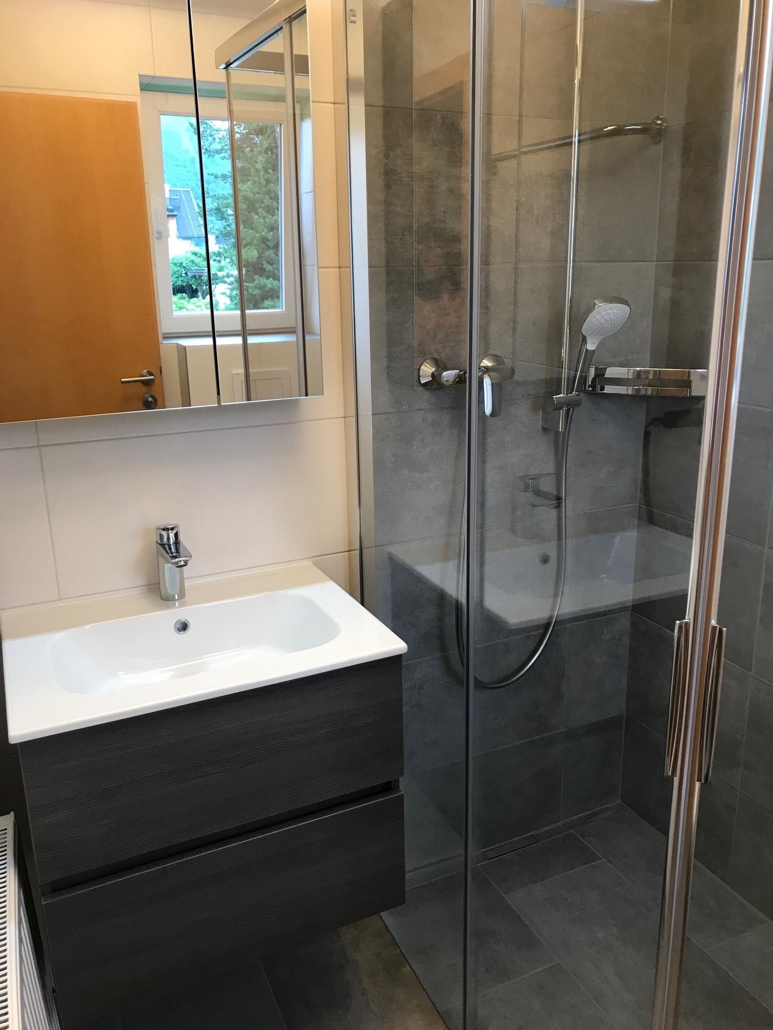 A modern bathroom with a shower and an elegant sink. The walls are tiled in light colors and there is a window for natural light.