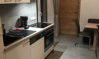 A modern kitchen with bright cabinets, a stove, and a dining area. The walls are simple, and a wooden door leads outside.