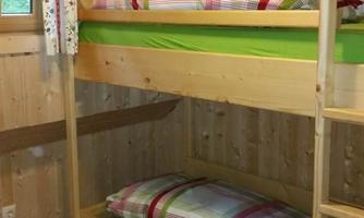 A cozy room with wooden bunk beds. The walls are made of wood and there is a window with curtains.