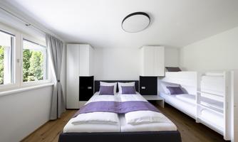 A modern bedroom with a double bed and a bunk bed. Bright walls and large windows create a friendly atmosphere.