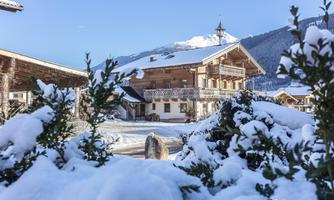 A beautiful, snow-covered wooden house in a picturesque winter landscape. The surroundings offer a calm, alpine atmosphere with mountains in the background.