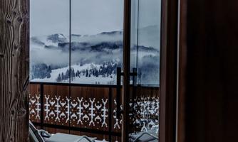 A window view of a snow-covered mountain with fog and a charming balcony. A relaxing atmosphere with a deck chair in the foreground.