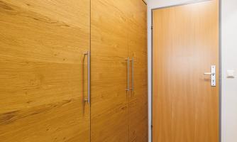 A modern hallway with a large wooden cabinet and a wood-colored door. The floor is made of light wood and there is plenty of light in the room.