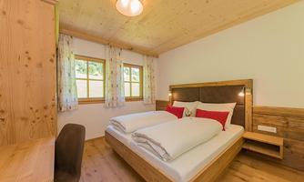 A cozy bedroom with a double bed and red pillows. Large windows provide plenty of daylight and a warm atmosphere.
