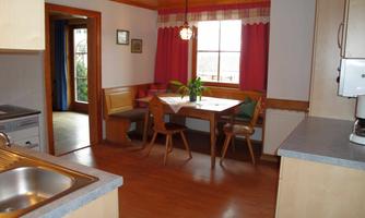 A cozy kitchen with a dining table and chairs. Red curtains and wooden details create a warm atmosphere.