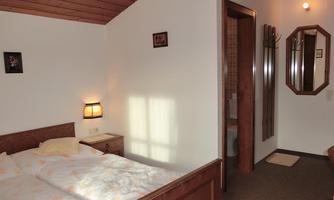 A cozy bedroom with two beds, a nightstand, and a lamp. In the background, a bathroom and a mirror are visible.