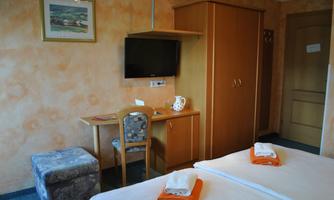 A simple and cozy room with two beds and towels. There is a table, a TV, and a wardrobe.