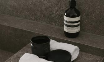 A stylish bathroom with black toiletries and white towels. The surfaces are made of elegant gray material.