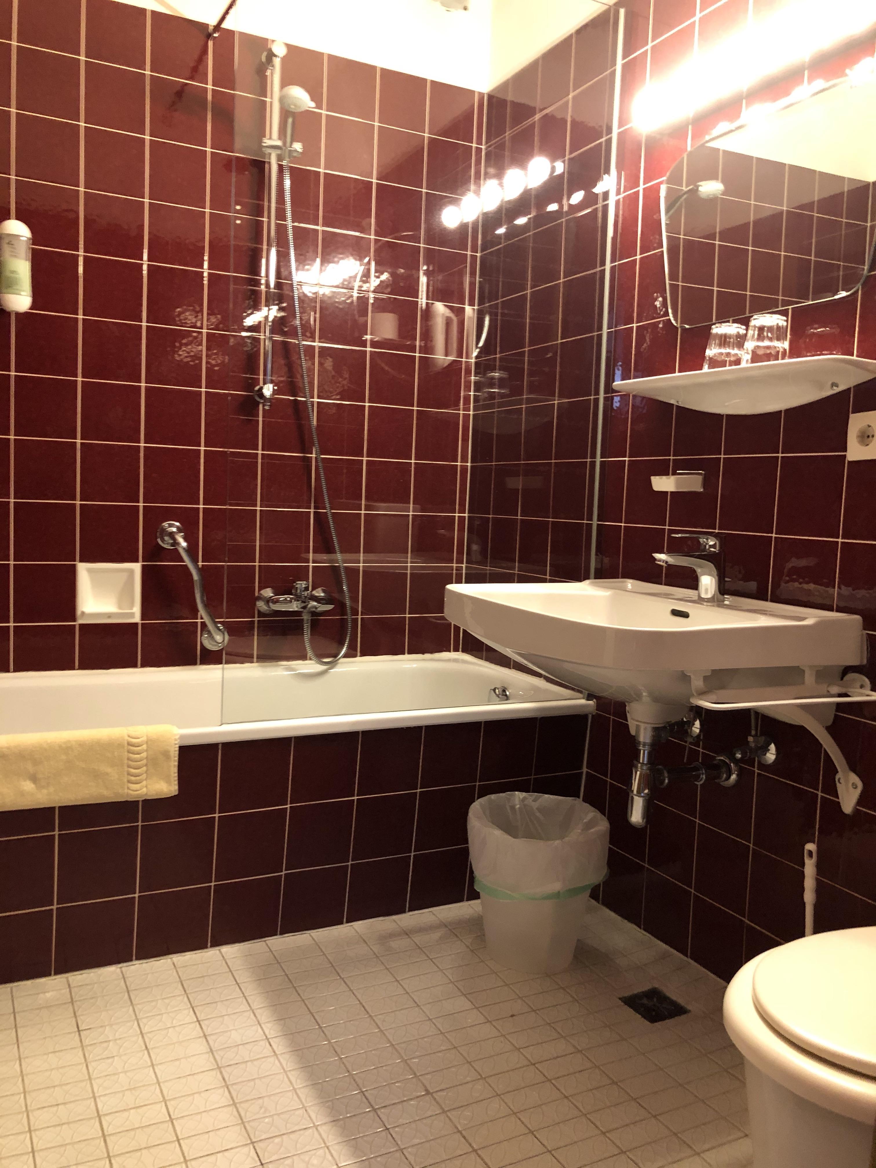 A modern bathroom with red tiles. There is a bathtub, a sink, and a toilet.