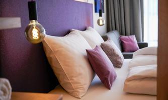 A stylish bedroom with a purple headboard and cozy pillows. Soft lighting and modern decor create an inviting atmosphere.