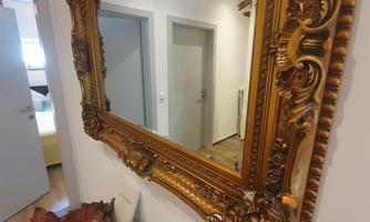 A beautiful golden frame with a mirror. Beneath it, some brochures lie on a wooden tray.