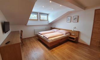 A modern bedroom with wooden flooring and two single beds. There is a window with natural light and simple furniture.