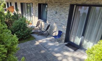 A terrace with two chairs and plants all around. The windows of the building are clearly visible and the ground is made of cobblestones.