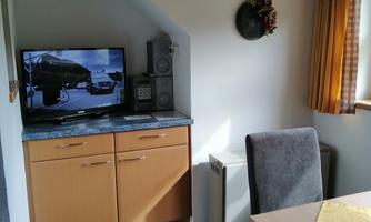 A cozy dining area with a table and chairs. In the background, there is a TV on a wooden sideboard.