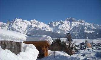 A snowy mountain landscape with majestic peaks in the background. In the foreground, a traditional building and snow-covered trees can be seen.