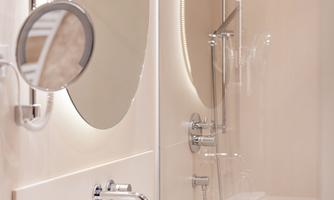 A modern bathroom with a large mirror and an elegant shower. The soft colors and clear furnishings create an inviting atmosphere.