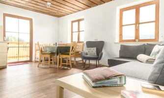 A bright and inviting living room with a wooden ceiling. There is a dining area and a cozy sitting space overlooking the window.