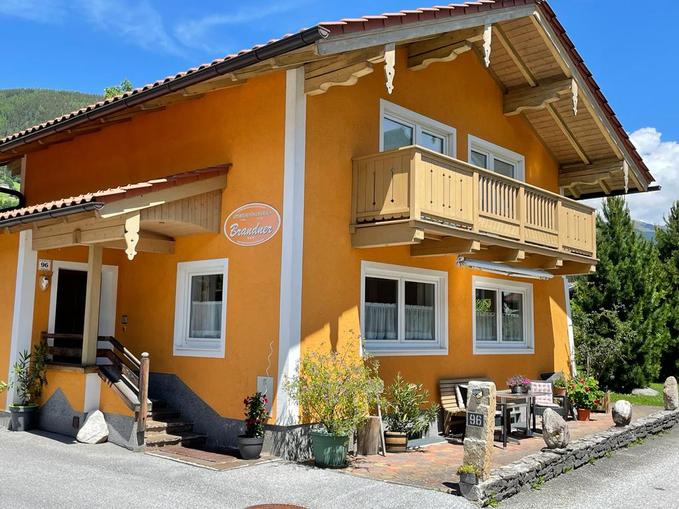 A charming orange house with a balcony.
Surrounded by plants and a green landscape background.